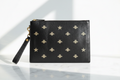 Elegant bright editorial view of Gucci black leather wristlet clutch with gold embossed bee and star motifs on white marble